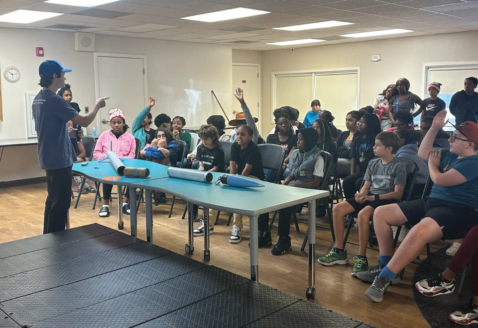 A team member showing rockets to a classroom of students with their hands raised